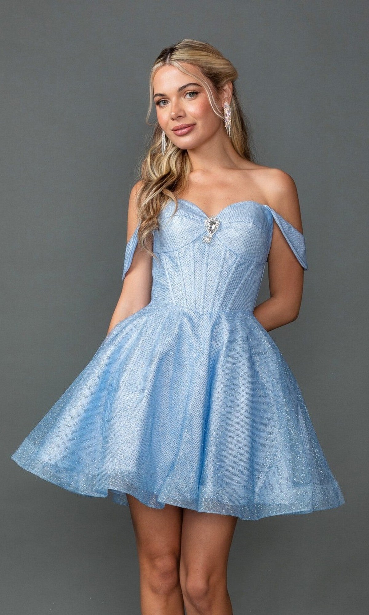 A woman models the Dancing Queen 3425 Short Prom Dress—light blue, off-the-shoulder with a sparkly fitted bodice and flared skirt—against a plain gray background.